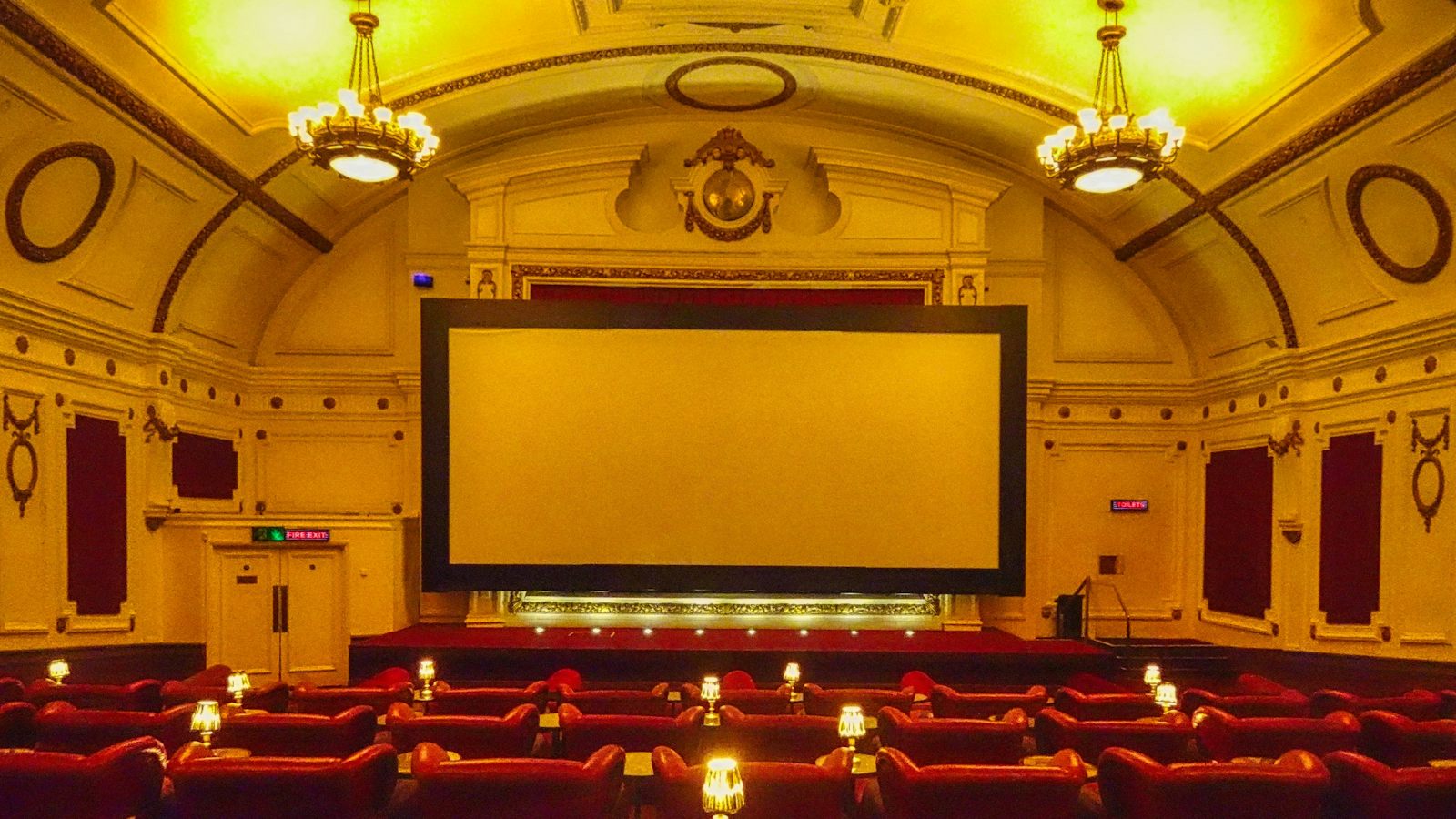 Stara bioskopska sala sa crvenim sedištima i platnom