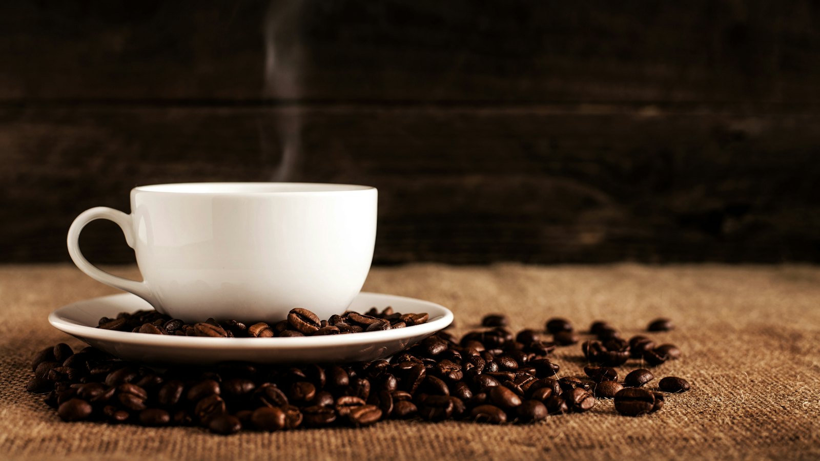 Šolja vruće kafe na tanjiriću punom zrna kafe
